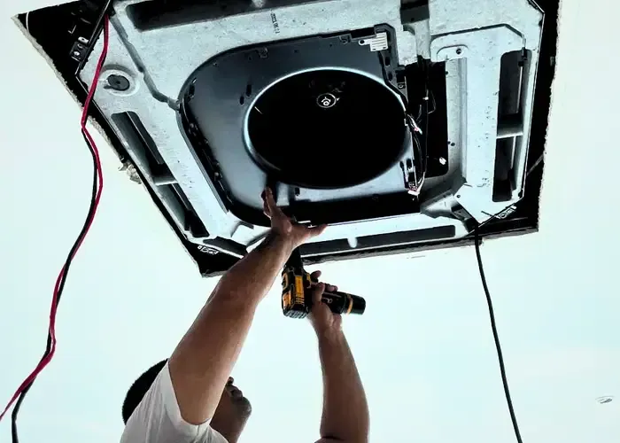 Técnico revisando con un taladro un aire acondicionado tipo cassette en el techo